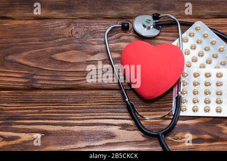 Un cuore con uno stetoscopio si trova su uno sfondo di legno. Cuore sano. Foto Stock