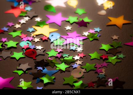 Confetti sparsi su uno sfondo nero da tavolo. Stelle e altre forme colorate realizzate in lamina multicolore. Foto Stock