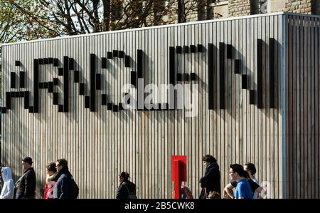 Il segno di illusione ottica in legno del centro artistico di Arnolfini e galleria con persone che passano sotto, Bristol, Avon, Inghilterra, Regno Unito Foto Stock