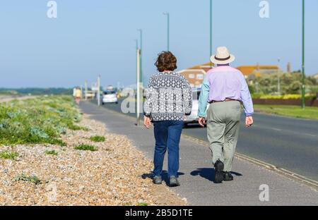 Una coppia anziana che si prende una passeggiata mattutina lungo una strada di fronte al mare in estate nel Regno Unito. Foto Stock