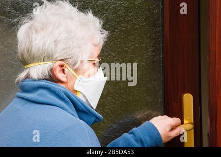 Una donna anziana anziana che va all'esterno indossando una maschera chirurgica che copre il naso e la bocca per proteggere contro i germi allergenici e Covid-19 Gran Bretagna Foto Stock