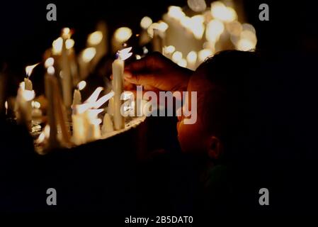 Un ragazzo non identificato accompagna i suoi genitori, illuminando le candele prima di una preghiera al cimitero della Cattedrale di Larantuka, una parte della Commemorazione del Venerdì Santo. Foto Stock
