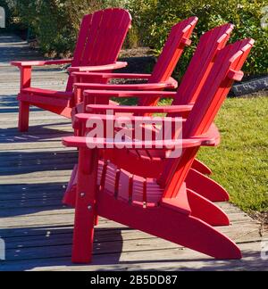 Quattro sedie rosse Adirondack luminose sedute sul molo di fronte alla stessa direzione Foto Stock