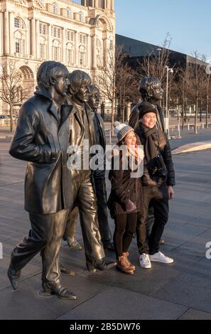 Coppia asiatica che si posa di fronte alla statua dei Beatles scolpita da Andrew Edwards a Pierhead a Liverpool Foto Stock