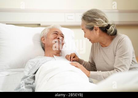 donna asiatica amorevole e premurosa che visita e parla con il marito ricoverato al letto Foto Stock