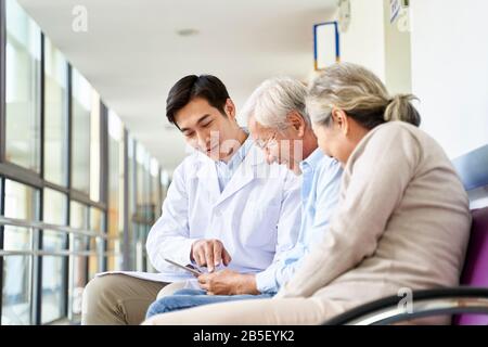 giovane medico asiatico che discute il risultato del test e la diagnosi con i pazienti anziani di coppia che usano la tavoletta digitale nel corridoio dell'ospedale Foto Stock