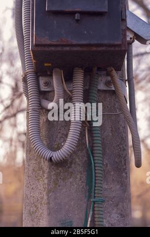 Montante in calcestruzzo con un vecchio quadro elettrico. Pannello elettrico in metallo arrugginito su un montante stradale. Apparecchiature elettriche obsolete. Vista laterale. Messa a fuoco selettiva Foto Stock