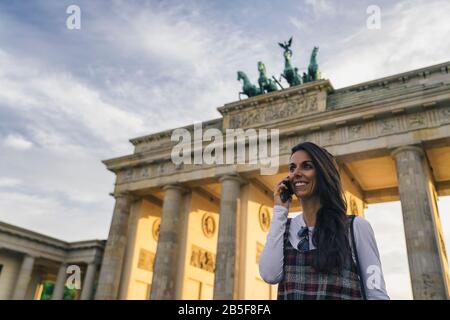 Sorridente giovane e giovane donna che parla su un telefono cellulare nella porta di Brandeburgo a Berlino, Germania. Foto Stock