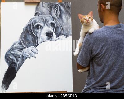 Un dipinto acrilico un uomo portare cane beagle con amore su tela bianca, mentre un artista portare gatto davanti alla sua opera. Foto Stock