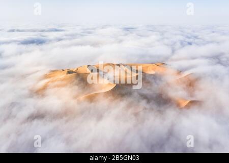 Veduta aerea di una gigantesca duna di sabbia circondata da nube di nebbia mattutina invernale. Liwa Desert, Abu Dhabi, Gli Emirati Arabi Uniti. Foto Stock