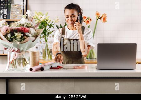 Fiorista femminile utilizzando il telefono cellulare presso negozio di fiori in piedi vicino al banco Foto Stock