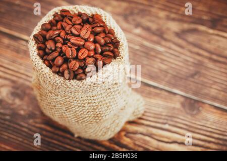 Chicchi di caffè in un sacchetto di burlap su uno sfondo di legno. Chicchi di caffè arrostiti Aromatici a contrasto morbido. La vista dall'alto. Foto Stock