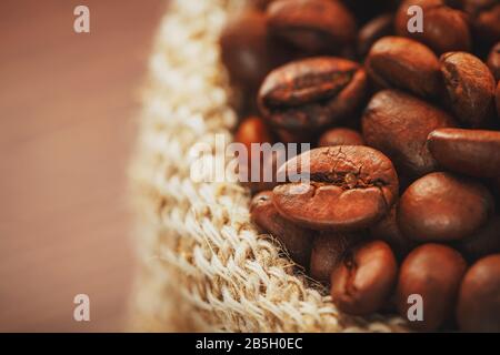 Caffè in grani in sacchetto di burlap su sfondo di legno. Contrasto morbido. Chicchi di caffè arrostiti aromatici. La vista dall'alto. Macro Foto Stock