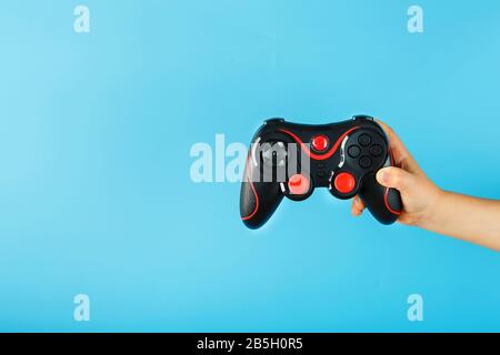 La mano di un bambino tiene trionfalmente il gamepad su uno sfondo blu. Concetto creativo minimalista della generazione più giovane di giocatori. Vincere online Foto Stock