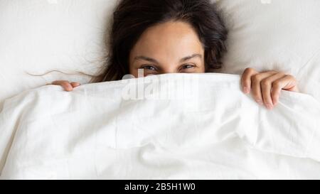 Sorridente giovane donna si nasconde sotto coperta svegliarsi Foto Stock