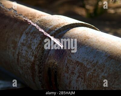 Un tubo di irrigazione che è così vecchio e arrugginito che ha mollato una perdita di gushing. Foto Stock