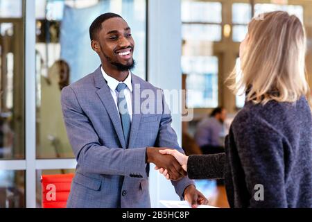 Ritratto di un giovane sorridente in abito da lavoro con cliente femminile o donna d'affari scuotendo le mani in ufficio riunione Foto Stock