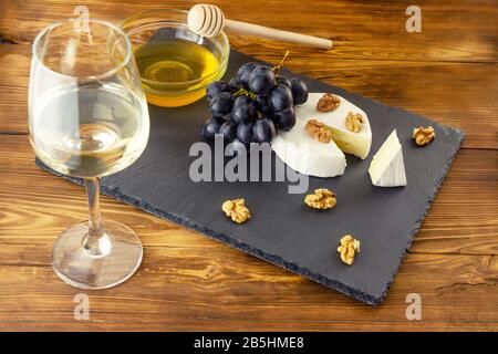 Formaggio Camembert, noci, miele e uva dolce sullo sfondo di un bicchiere di vino bianco secco e sfondo di legno con copyspace Foto Stock