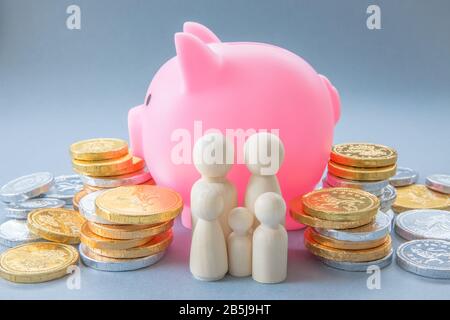 Un'immagine concettuale di una famiglia che sta davanti ad una grande banca rosa di Piggy e circondata da contanti e monete che rappresentano la banca di mamma e papà con c Foto Stock