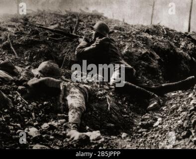 Durante la battaglia di Verdun nel febbraio 1916, un soldato tedesco che usa la copertura di una trincea danneggiata accanto al corpo di un soldato francese. Foto Stock