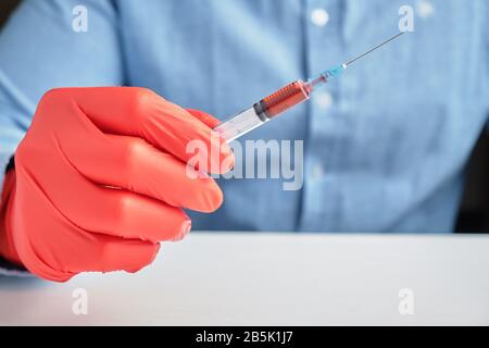 Una mano in guanti rossi contiene una siringa con un vaccino. Primo piano. Foto Stock