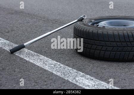 Una ruota piatta per auto e un cacciavite sono su una strada asfaltata. Servizio di automobile. Concetto di sostituzione degli pneumatici, Praga, marzo 2020 Foto Stock