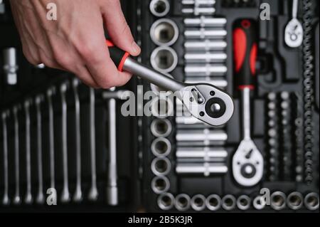 mano umana con attrezzo di riparazione per auto sullo sfondo del kit cassetta attrezzi Foto Stock