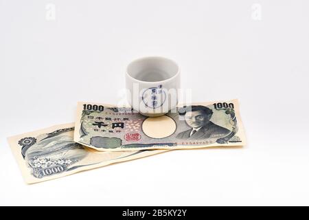 Concetto di viaggio del mondo con tazza bianca tradizionale di sake con scrittura giapponese e note di 1000 yen Foto Stock