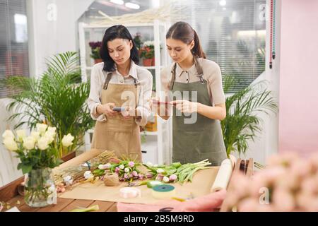 Girovita ritratto di due giovani donne che scattano foto di fiori per la promozione di media di piccola impresa mentre lavorano in negozio di fiori, copia spazio Foto Stock