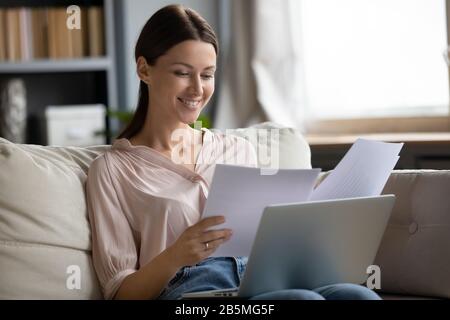 Giovane donna sorridente seduto sul divano, leggendo lettere di carta. Foto Stock