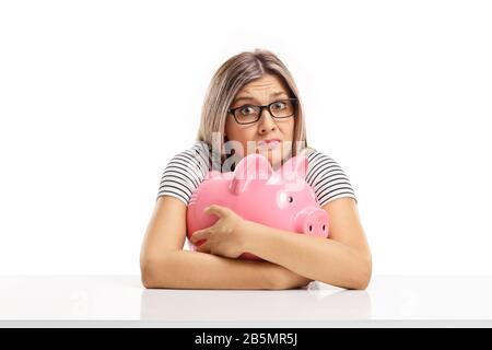 Giovane donna confusa che abbraccia un piggybank isolato su sfondo bianco Foto Stock