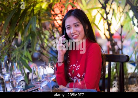 Una giovane donna vietnamita che indossa un tradizionale abito rosso Ao dai utilizzando il suo cellulare Foto Stock