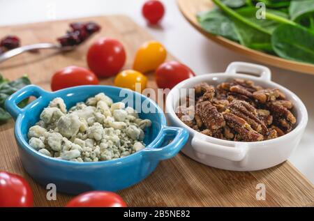 Ingredienti di insalata primo piano. Spinaci, pomodori, formaggio blu, noci pecan, mirtilli rossi su un tavolo da cucina Foto Stock