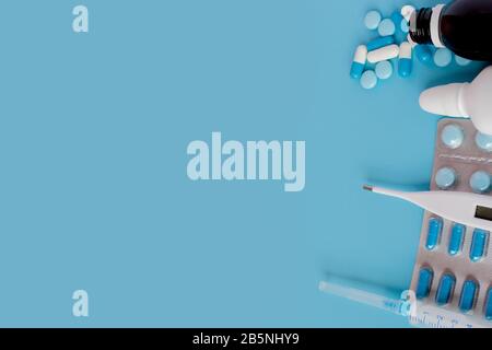 Il trattamento di raffreddori e influenza. Diversi medicinali, un termometro, spray da un naso chiuso e un dolore in una gola su uno sfondo blu. Spazio di copia Foto Stock