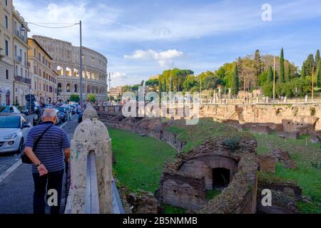 Edifici dell'antica Roma, vista sulla strada delle rovine di Ludo Magnus, Scuola di formazione dei grandi gladiatori, con Colosseo romano sullo sfondo, Roma, Italia. Foto Stock