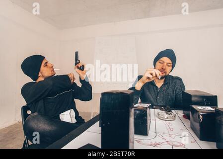 I capi pericolosi parlano in una stanza, fumando le sigarette e uno di loro sta tenendo una pistola Foto Stock
