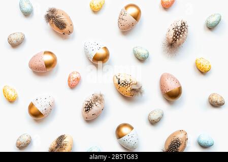 Vista dall'alto delle uova di Pasqua sparse colorate con vernice dorata in diversi modelli e colori. Sfondo bianco. Foto Stock