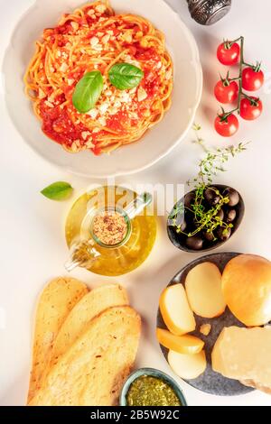 Cibo italiano top shot. Spaghetti, formaggio, pomodori, olive, olio d'oliva e pane su sfondo bianco Foto Stock