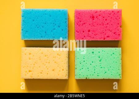 Spugne gialle, verdi, rosse, blu sullo sfondo di carta colorata, vista dall'alto. Foto Stock
