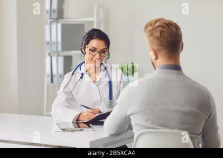 Terapista medico femminile allergista grave otolaringogo nutrizionista e paziente maschile seduto a un tavolo in un ufficio clinico Foto Stock