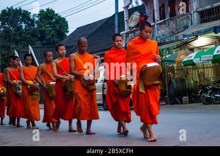 Giovani monaci indossando color ocra accappatoi raccogliendo elemosine (tak bat) a Luang Prabang, Laos. Nelle prime ore del mattino hanno il flusso fuori dai templi e o Foto Stock