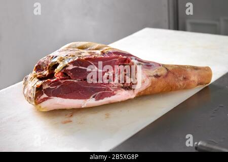 Pezzo di prosciutto crudo di carne di prosciutto in un macellaio, visto in primo piano sul tavolo da taglio bianco Foto Stock