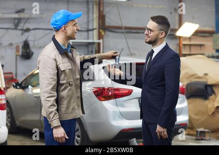 Vista laterale orizzontale del lavoratore di servizio automatico professionale che dà le chiavi dell'automobile al suo cliente dopo la riparazione della sua automobile Foto Stock