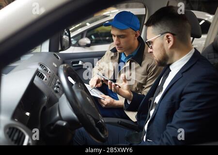 Orizzontale medio ritratto di specialista di servizio auto professionale e il suo cliente maschio seduto in auto che discute qualcosa Foto Stock