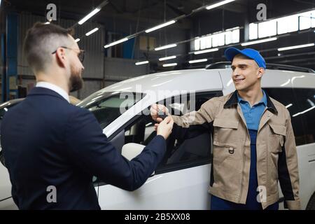 L'uomo irriconoscibile che indossa il vestito che dà le sue chiavi dell'automobile ai riparatore di servizio auto, colpo medio orizzontale Foto Stock