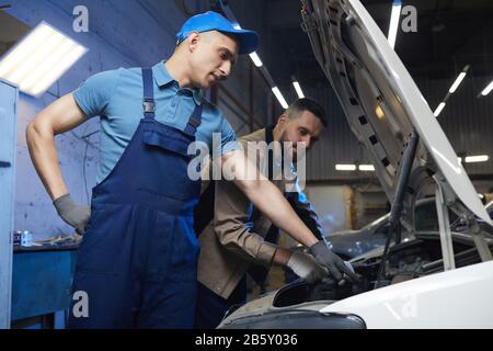 Orizzontale basso angolo medio lungo scatto di due meccanici professionisti auto indossando uniforme controllo dello stato del veicolo insieme, copia spazio Foto Stock