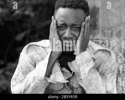 Faccia di giovane uomo africano senza tetto che guarda depresso in bianco e nero Foto Stock