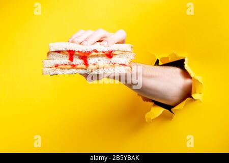Tenere un sandwich con carta gialla strappata sullo sfondo Foto Stock