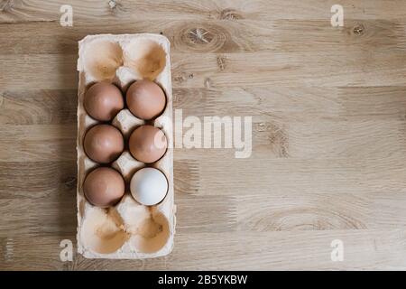 Sei uova di pollo in vassoio di cartone sul tavolo di legno. Uova crude in contenitori aperti di cartone. Primo piano. Tema di Pasqua. Disposizione piatta. Spazio di copia. Foto Stock