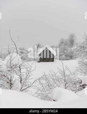 Minimalista paesaggio invernale con casa in legno in montagna innevata. Tempo attuale nuvoloso, fotografia di paesaggi Foto Stock